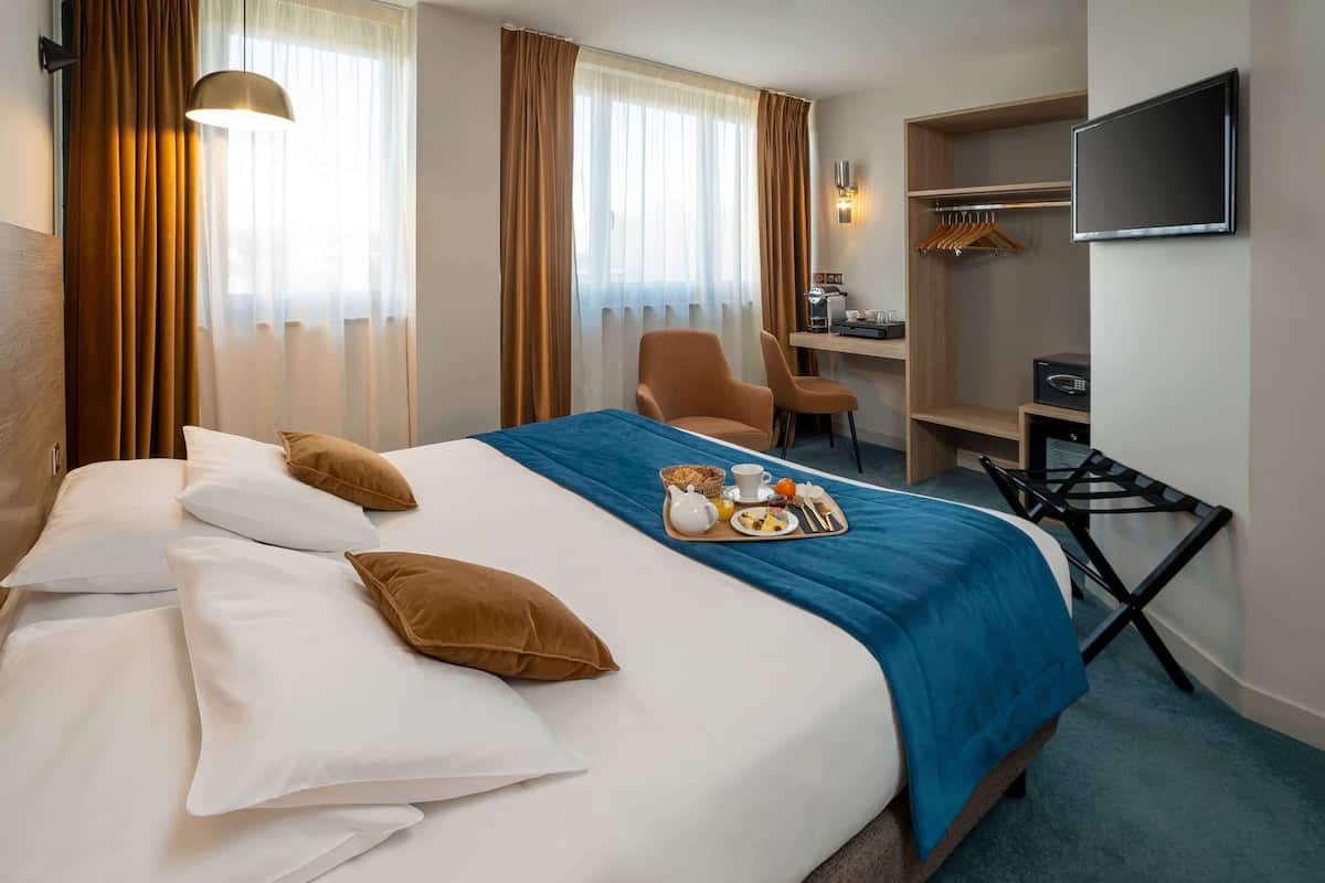 A hotel room with a bed, a desk, a chair, a TV, and a breakfast tray on the bed.