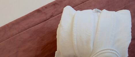 Una cama bien hecha con un cabecero marrón, una almohada blanca y otra almohada marrón. Una toalla blanca está colocada sobre la cama.