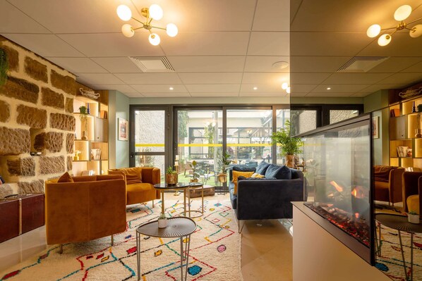 A modern living room with a stone wall, comfortable seating, a glass fireplace, and large windows offering a view of the outside.