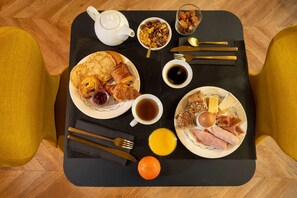 A breakfast tray with pancakes, croissants, ham, eggs, orange juice, and coffee.