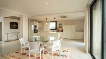 A modern kitchen with white cabinets, a glass dining table, and white chairs.