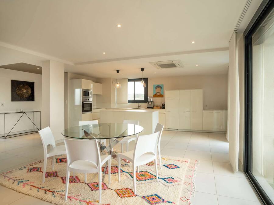 A modern kitchen with white cabinets, a glass dining table, and white chairs.