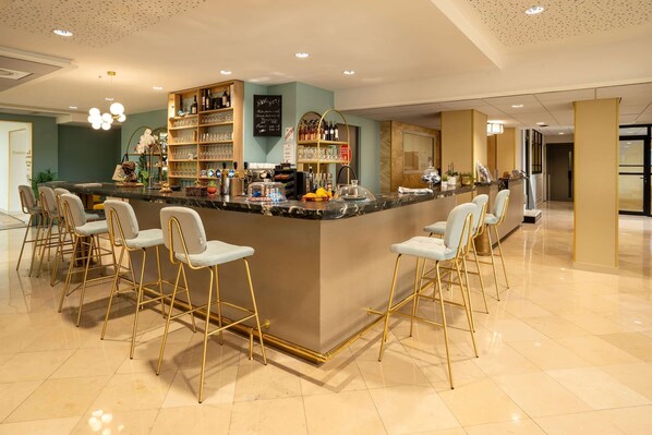 A bar area with a marble counter, gold chairs, and shelves with bottles and glasses.