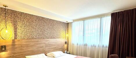 A hotel room with a large bed, a small side table, a chair, and a desk.