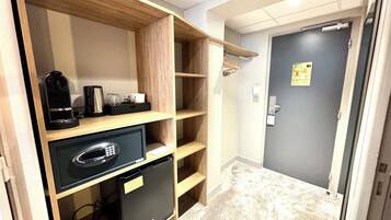 Camera d'albergo compatta con angolo cottura, un piccolo frigorifero, una macchina per il caffè e una scaffalatura in legno.