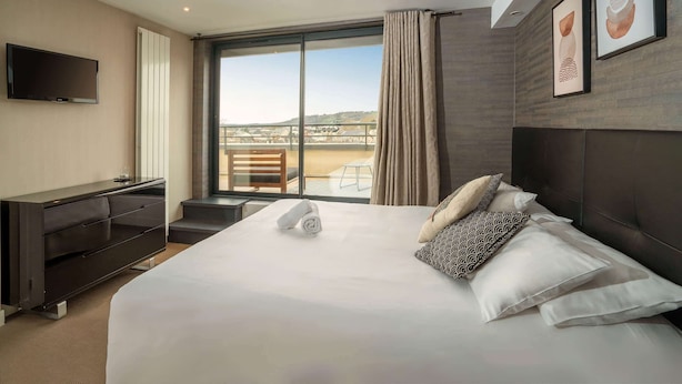 A hotel room with a large bed, a flat-screen TV, a desk, and a balcony with a view.