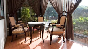 A room with a round table and four chairs, large windows with curtains, and a view of greenery outside. - Happiness Hotel (Taipei)