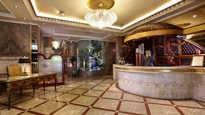 A lobby with a marble floor, a reception desk, a chandelier, and a reception area with a man on the phone. - Happiness Hotel (Taipei)