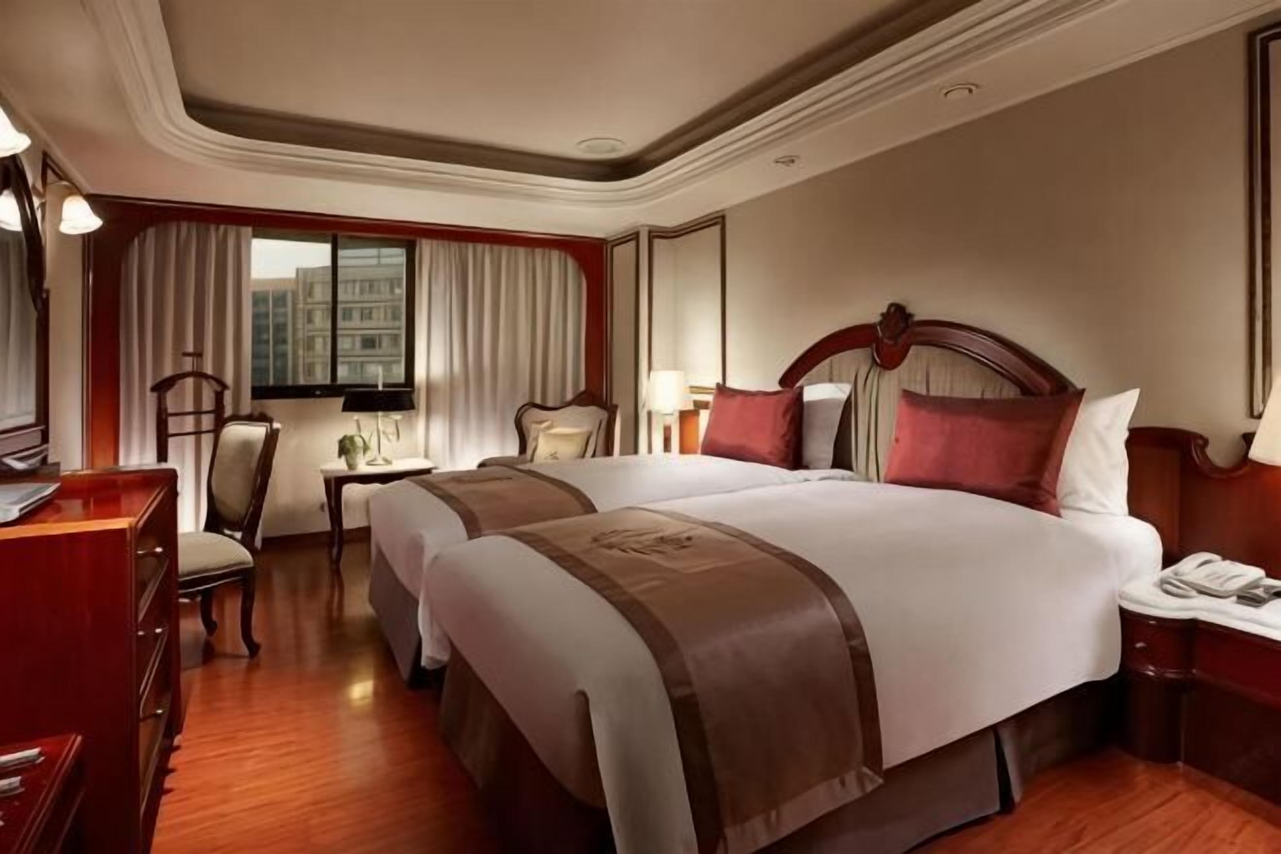 A hotel room with a double bed, a desk with a chair, a lamp, and a window with curtains.