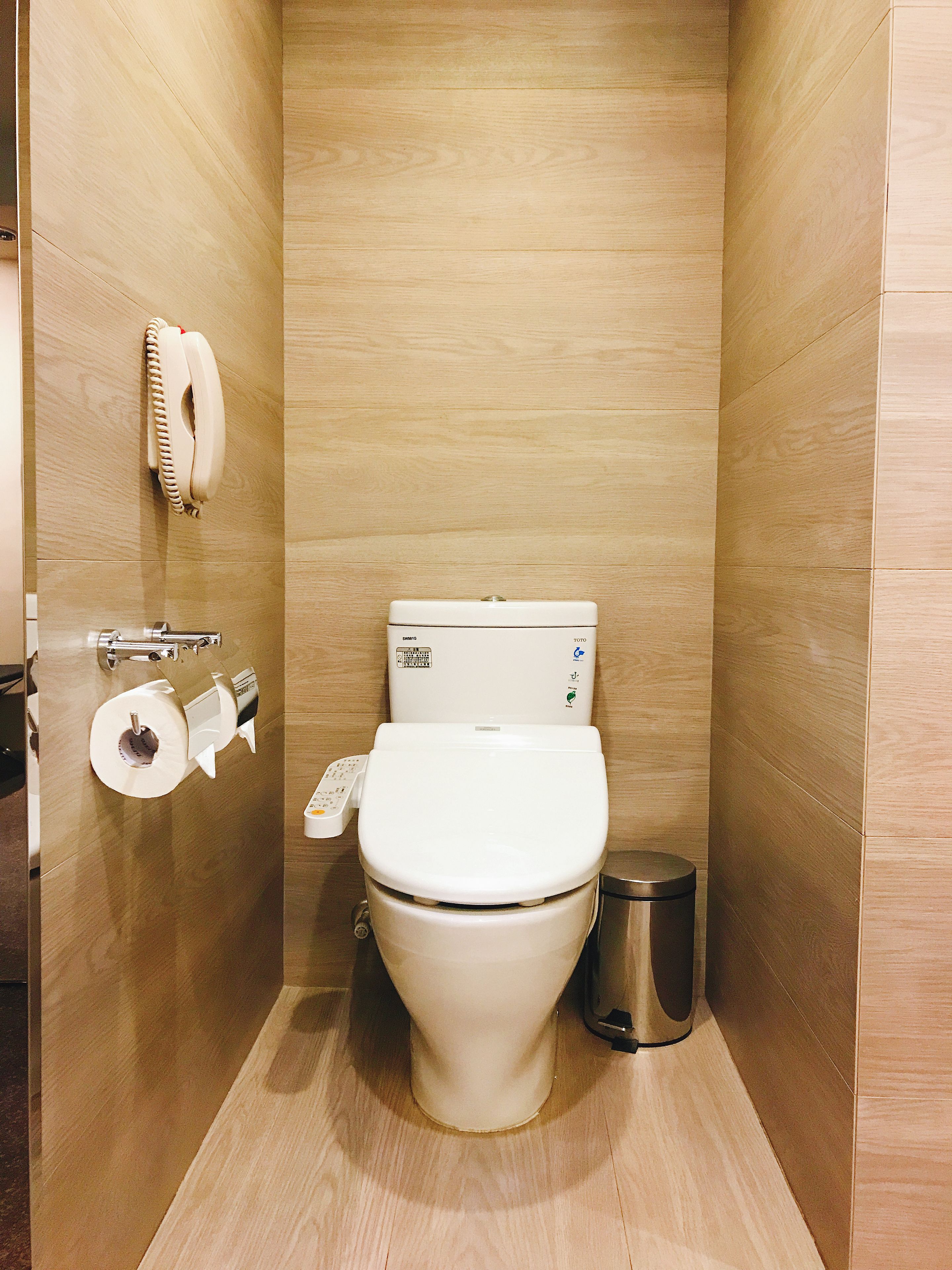 Un baño moderno y compacto con inodoro, secador de manos y cubo de basura.