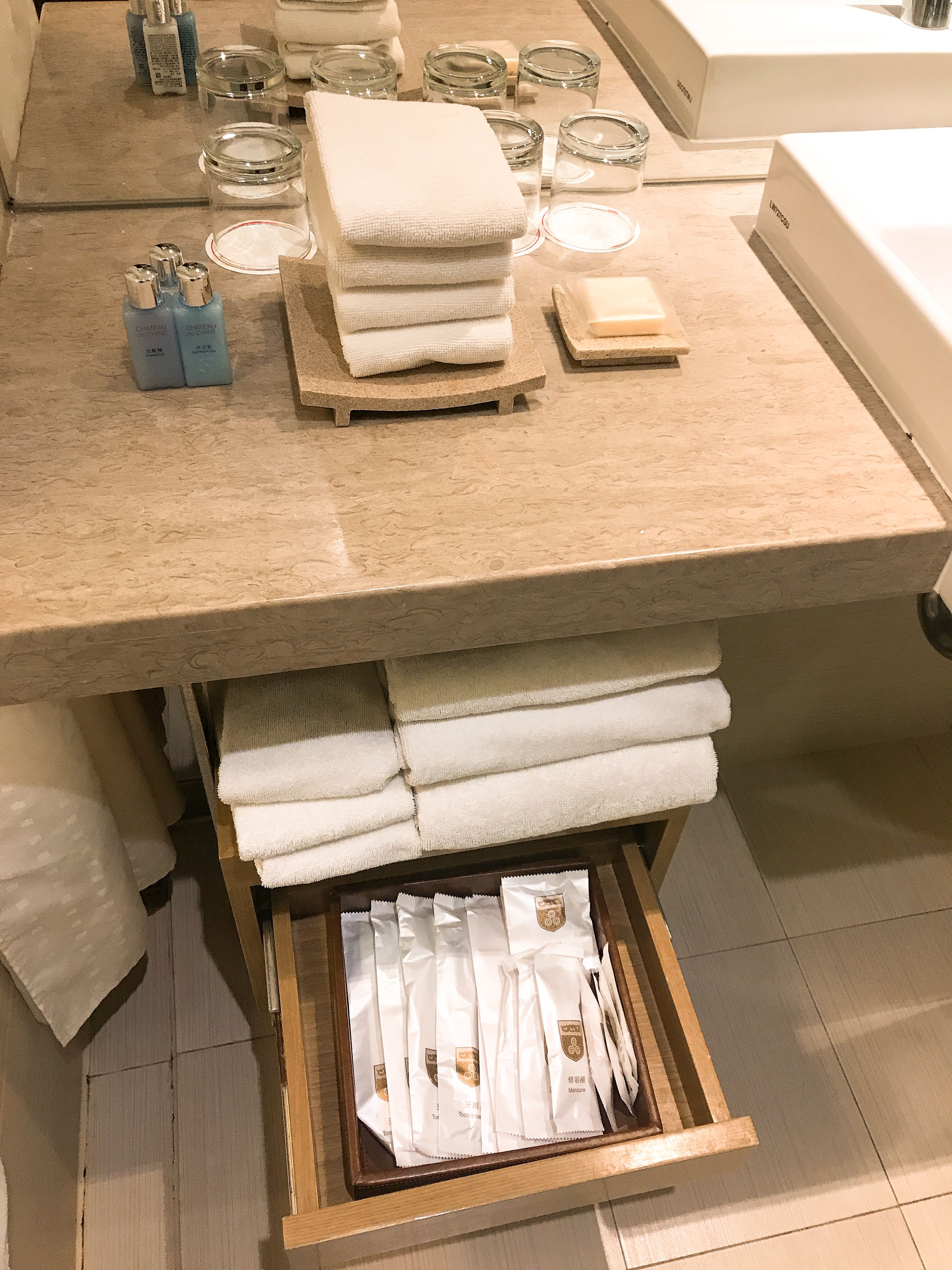 A bathroom counter with neatly stacked towels, a soap dish, and a drawer with packaged toiletries.