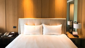 Une chambre d’hôtel avec un grand lit, une table de chevet avec une lampe, un téléphone et une petite table de chevet avec un livre et une boîte de mouchoirs.