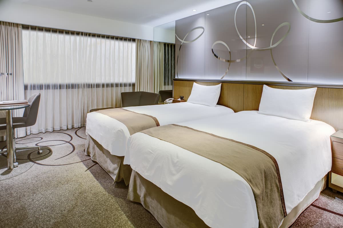 A hotel room with two beds, a desk, and a chair.