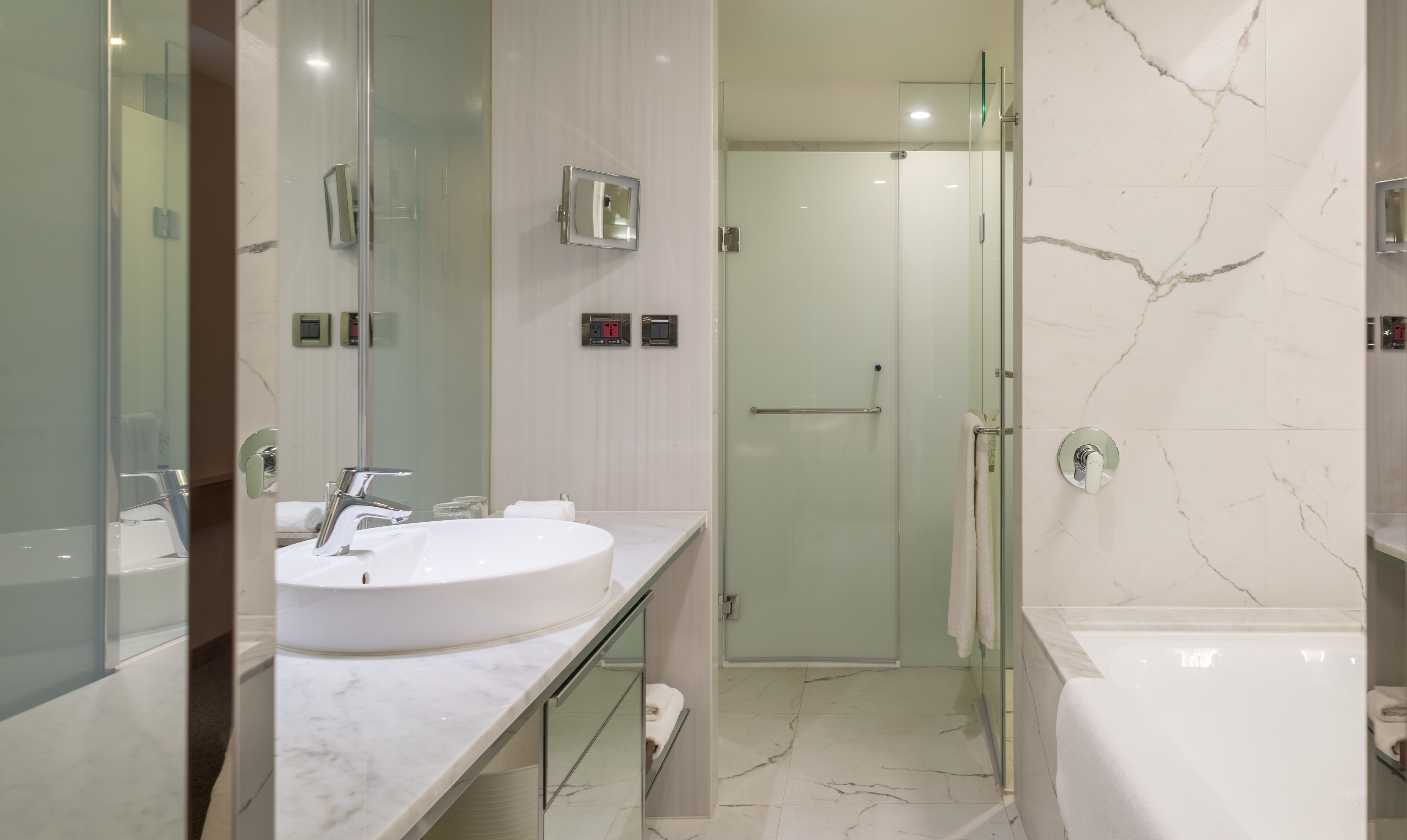 A modern bathroom with a large white sink, a glass shower enclosure, and marble flooring.