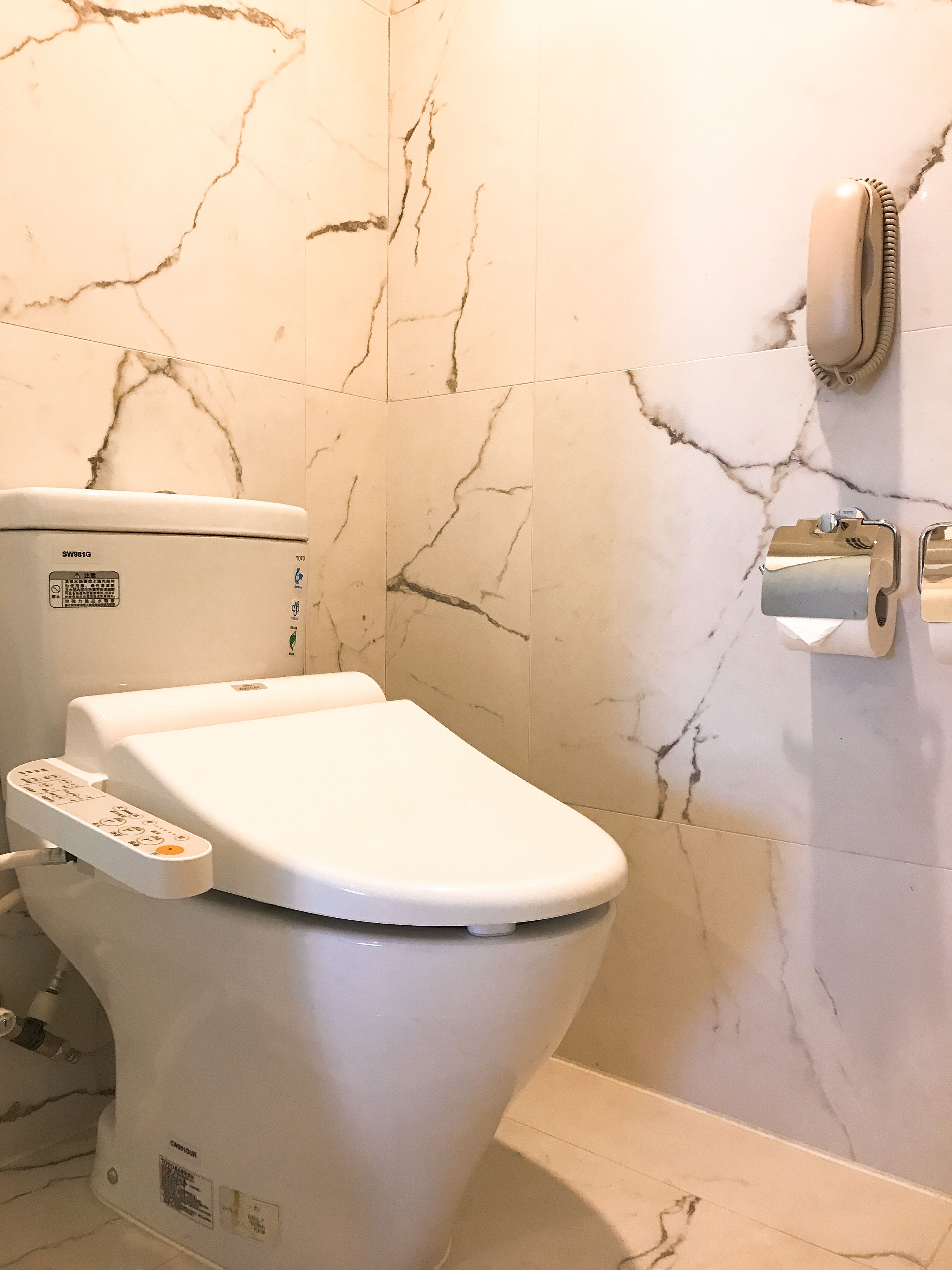 A modern bathroom with a white toilet, a control panel, and a hand dryer on the wall.