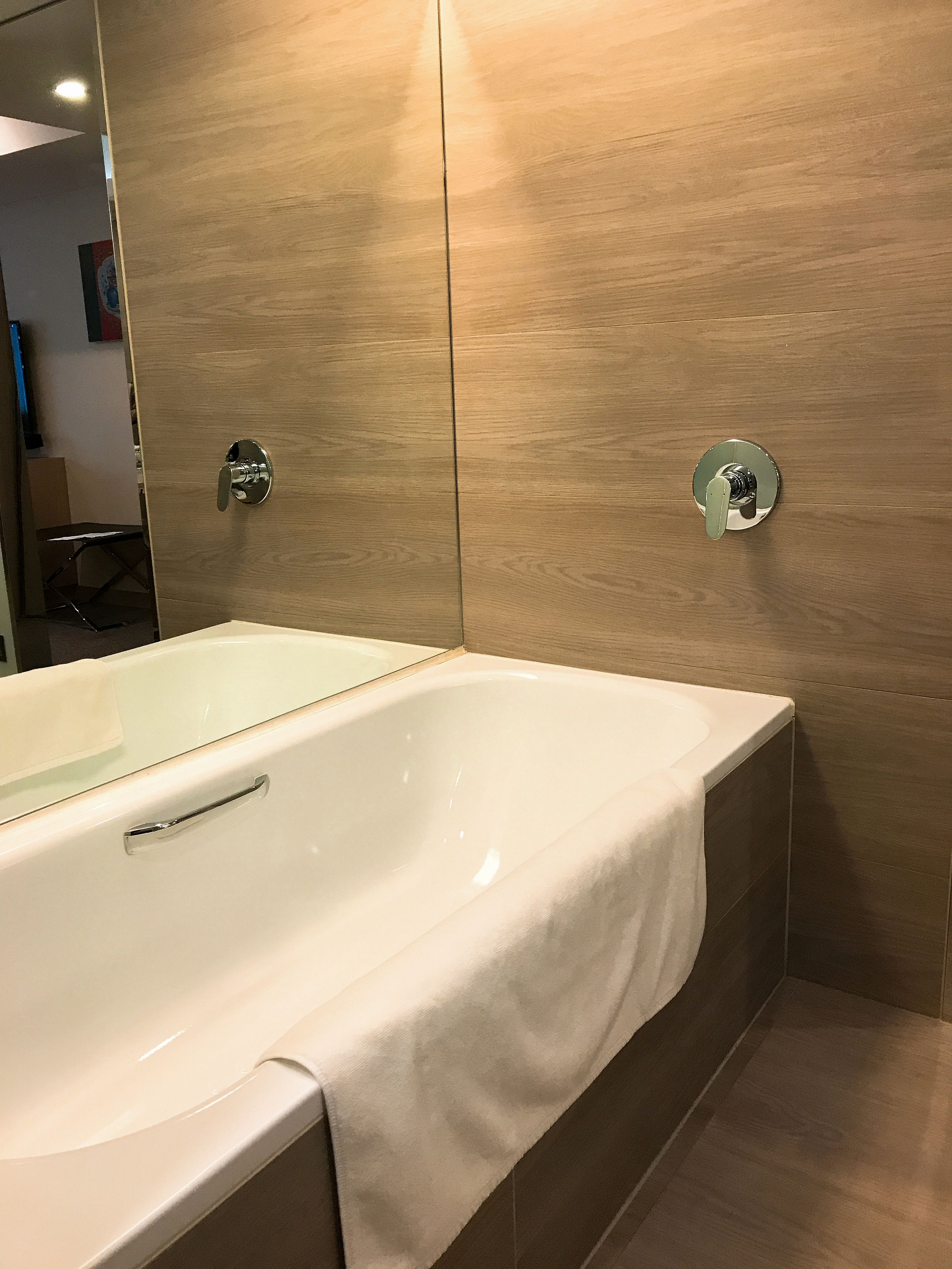 Un baño moderno con una bañera grande, paneles de madera y un espejo.