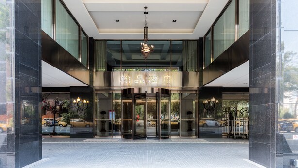 L’entrée d’un hôtel au design moderne, avec une façade en verre, un lustre central et une enseigne au-dessus des portes.