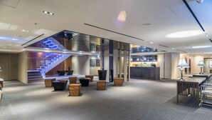 Un hall d’entrée moderne avec un escalier en verre, un espace salon et un comptoir d’accueil.