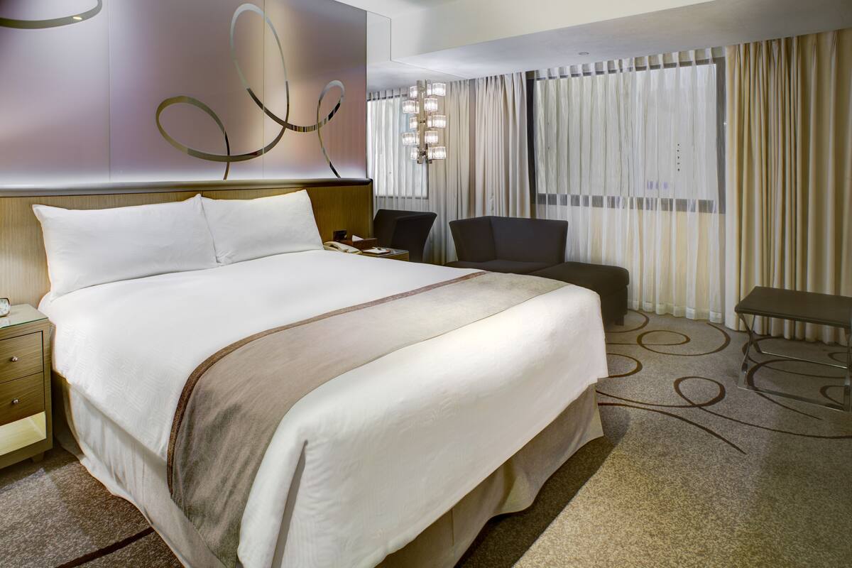 A hotel room with a large bed, a desk, a chair, and a lamp.