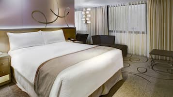 A hotel room with a large bed, a desk, a chair, and a lamp.