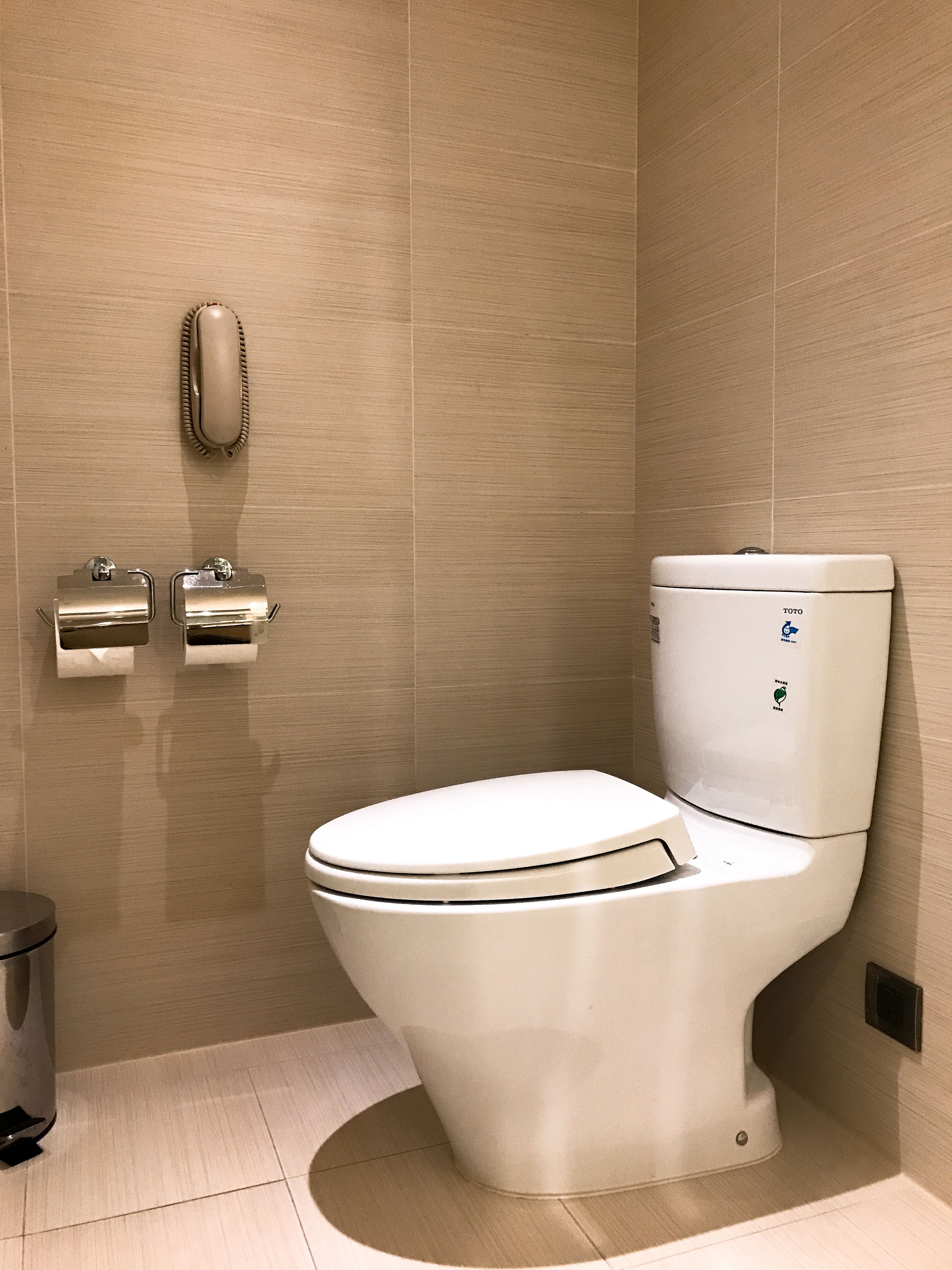 A modern bathroom with a white toilet, a paper towel dispenser, and a hand dryer mounted on the wall.