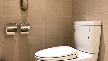 A modern bathroom with a white toilet, a paper towel dispenser, and a hand dryer mounted on the wall.