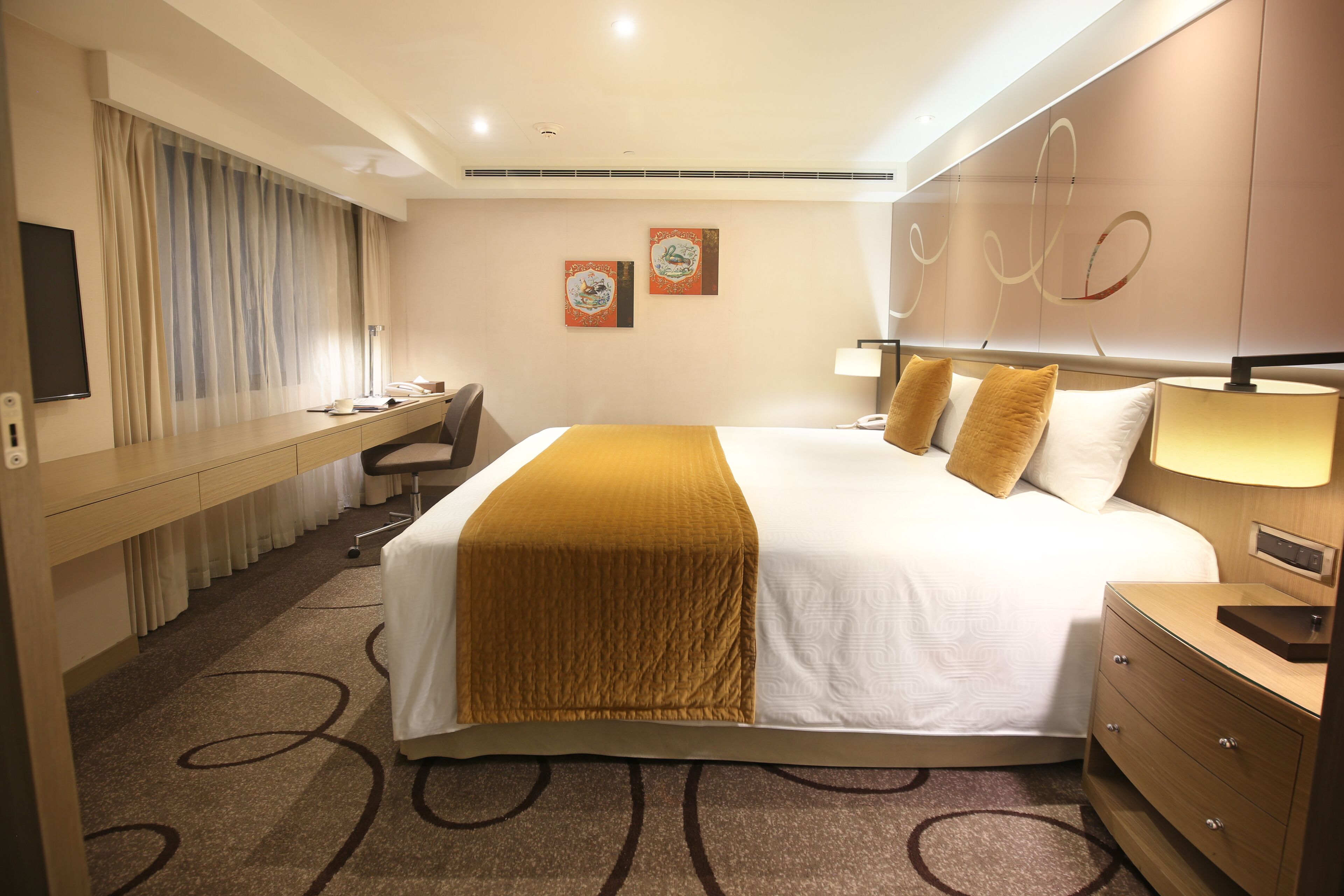 A hotel room with a large bed, a desk, a chair, and a bedside table.