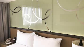 Une chambre d’hôtel avec un lit, une table de chevet avec un téléphone, une lampe et un grand miroir orné de motifs abstraits.