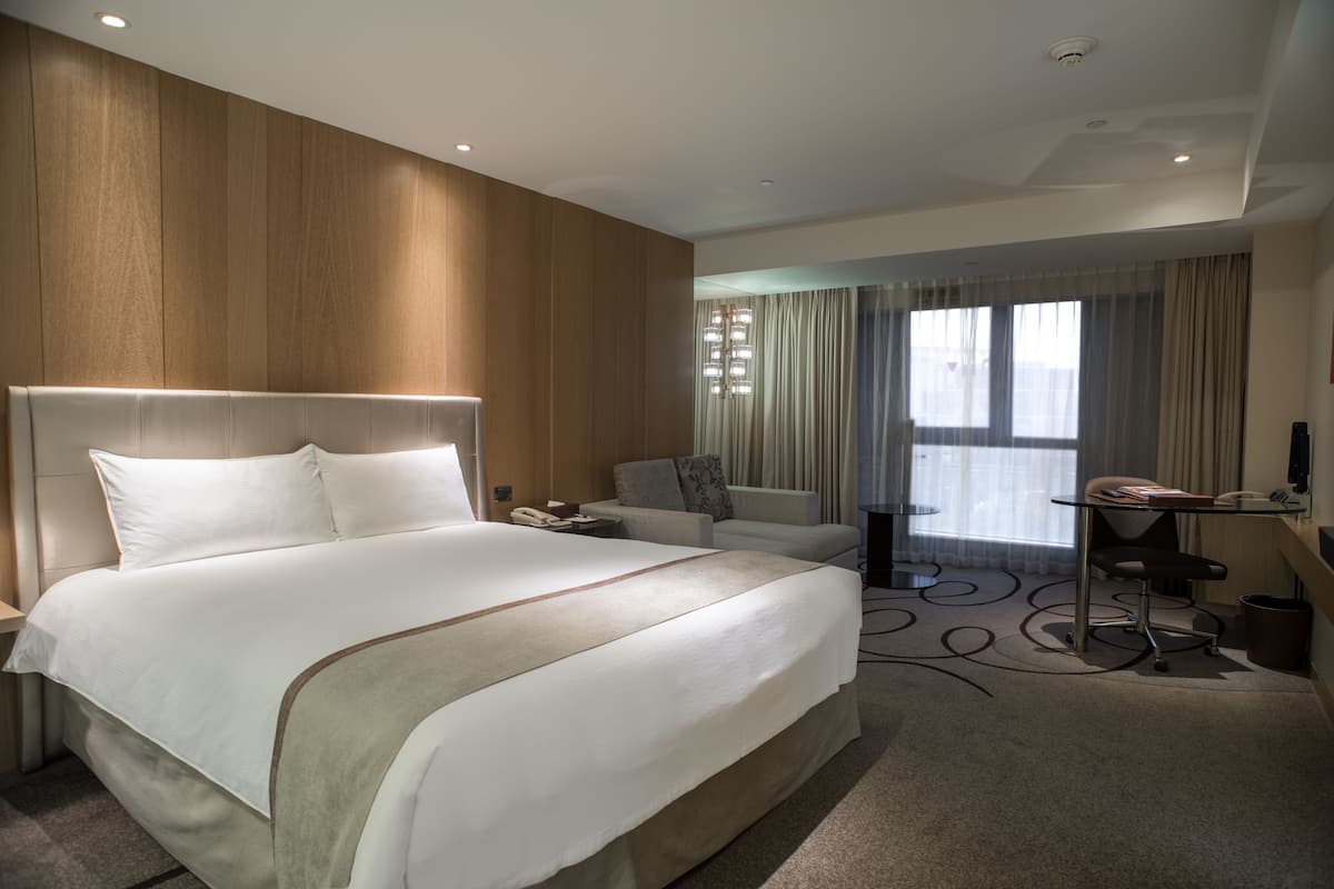 A hotel room with a large bed, a desk, a chair, and a view of the outdoors through a window.