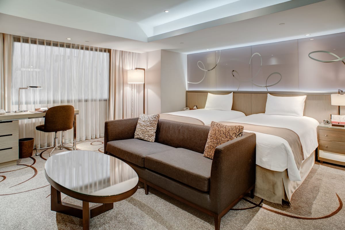 A modern hotel room with a large bed, a sofa, a desk, and a round table.