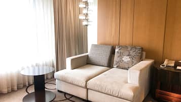 A modern hotel room with a beige sofa, two patterned cushions, a small round table, and a telephone on a wooden side table.