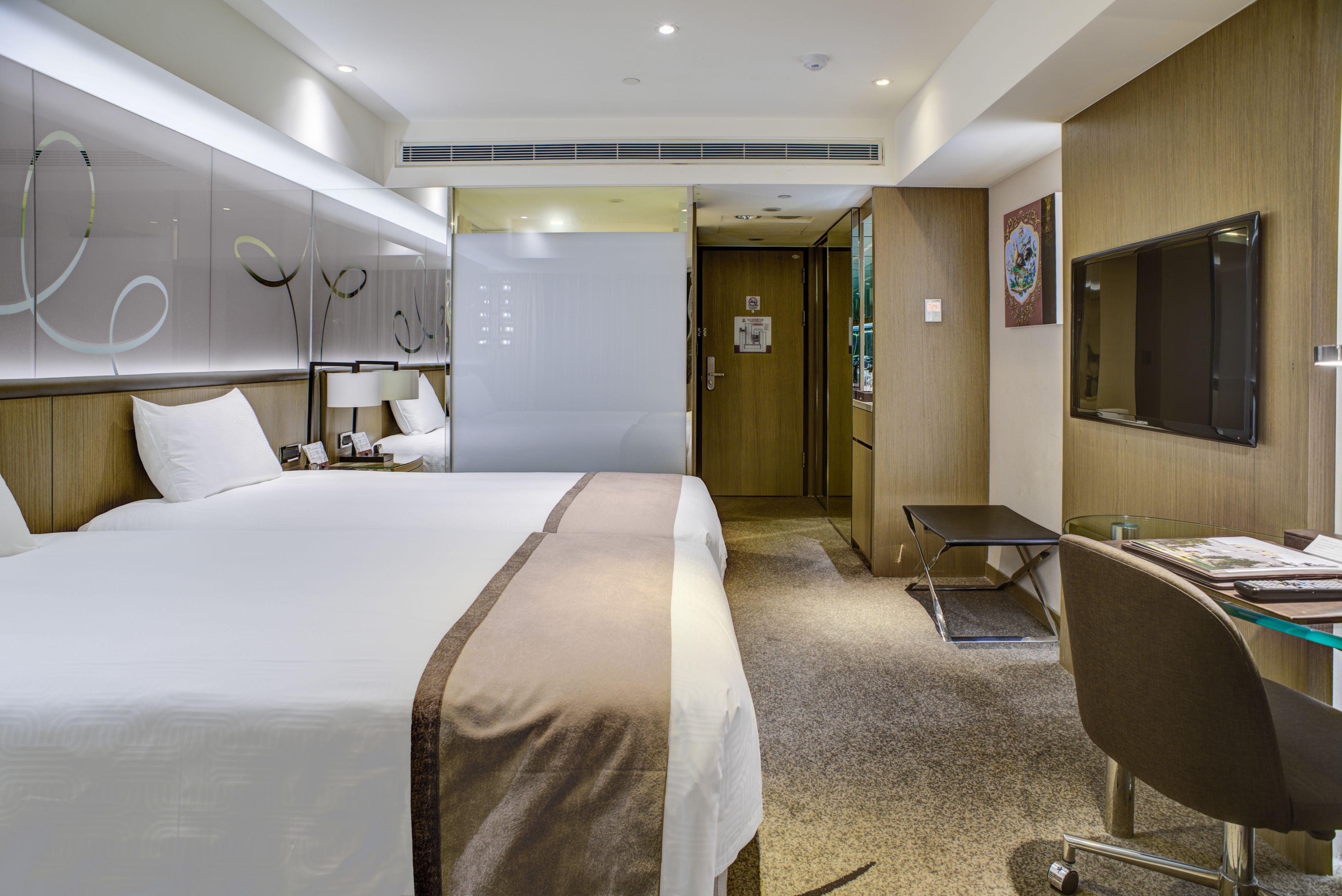 A hotel room with a large bed, a desk with a chair, a TV, and a door leading to another room.
