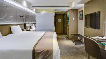 A hotel room with a large bed, a desk with a chair, a TV, and a door leading to another room.