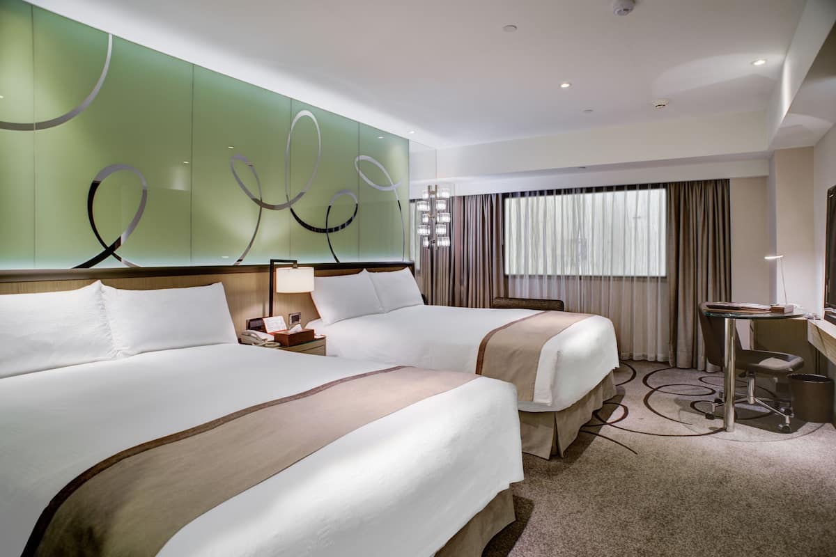A hotel room with two beds, a desk, a chair, and a large window with curtains.