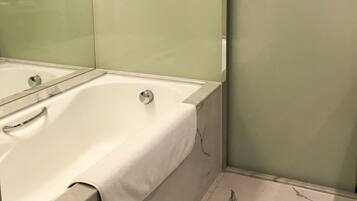 A modern bathroom with a large bathtub, a glass shower enclosure, and a marble floor.