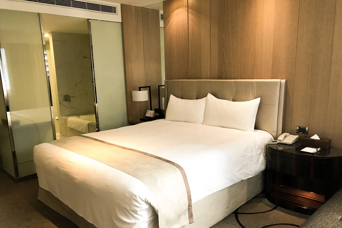 A hotel room with a large bed, a bedside table with a lamp, a phone, and a tissue box.