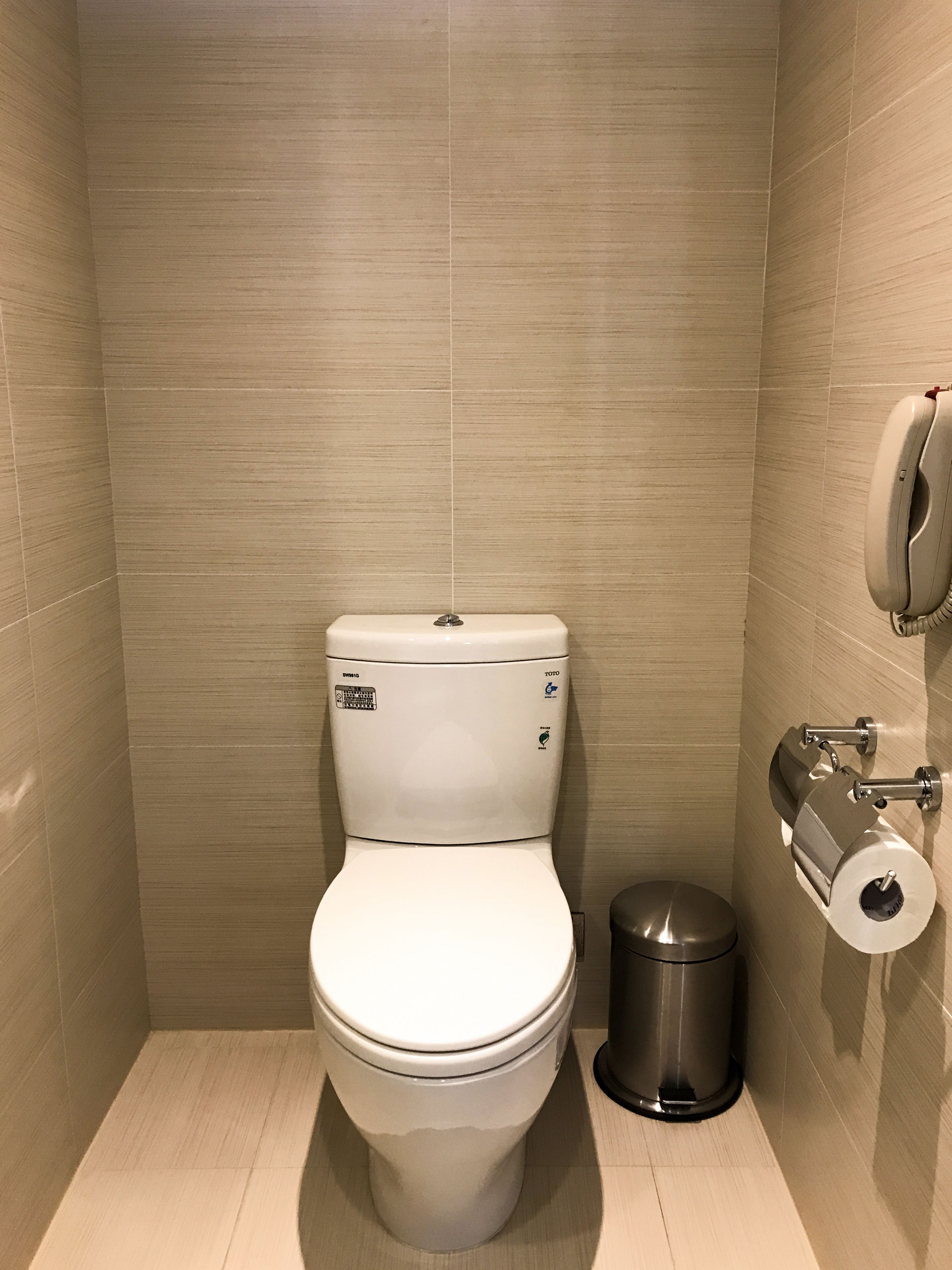 Un baño pequeño y moderno con inodoro blanco, un cubo de basura y un dispensador de papel higiénico en la pared.