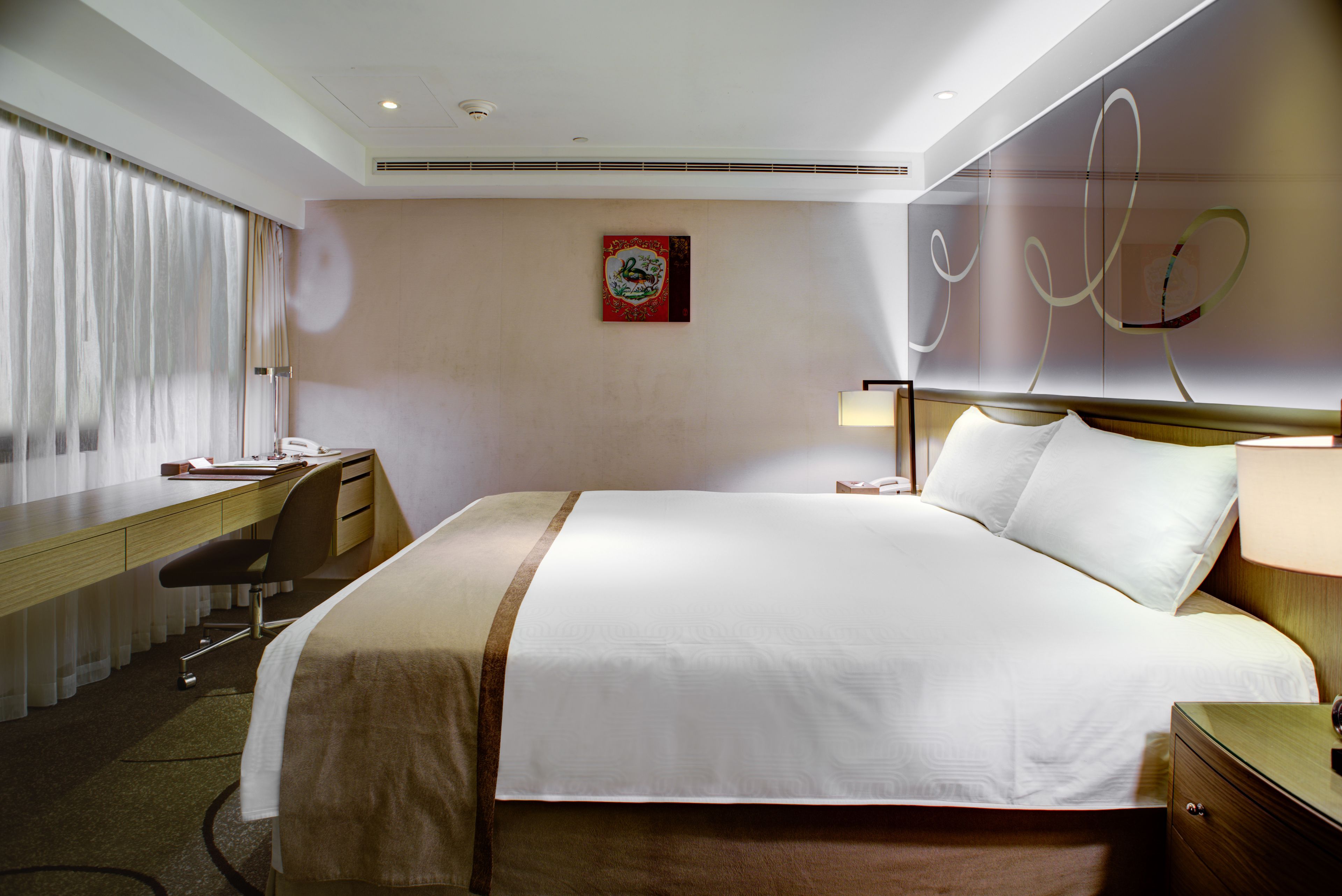 Habitación de hotel con una cama grande, un escritorio con silla, una mesita de noche y una obra de arte colgada en la pared.