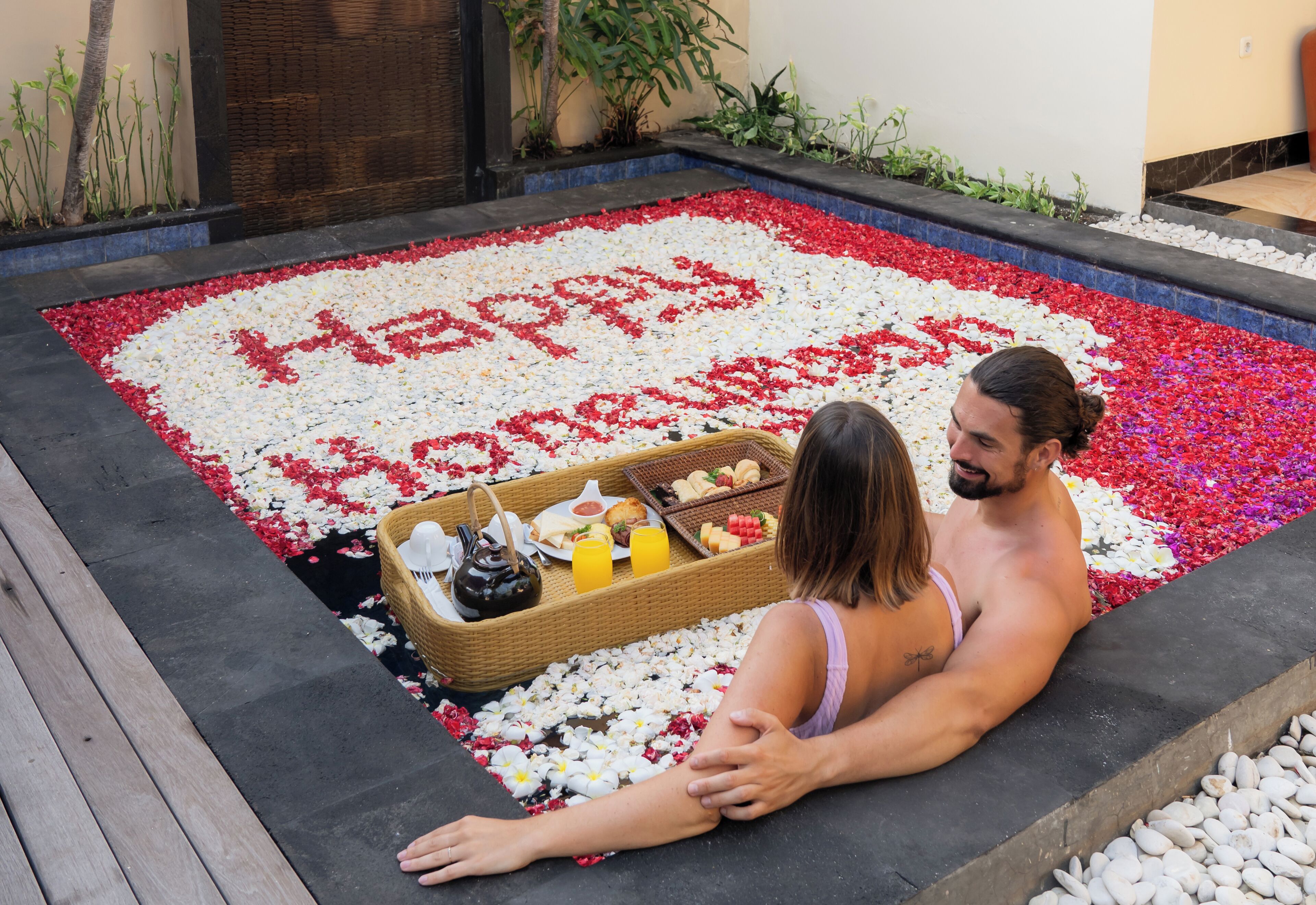 A couple sitting on a stone bench with a flower bed in front of them.