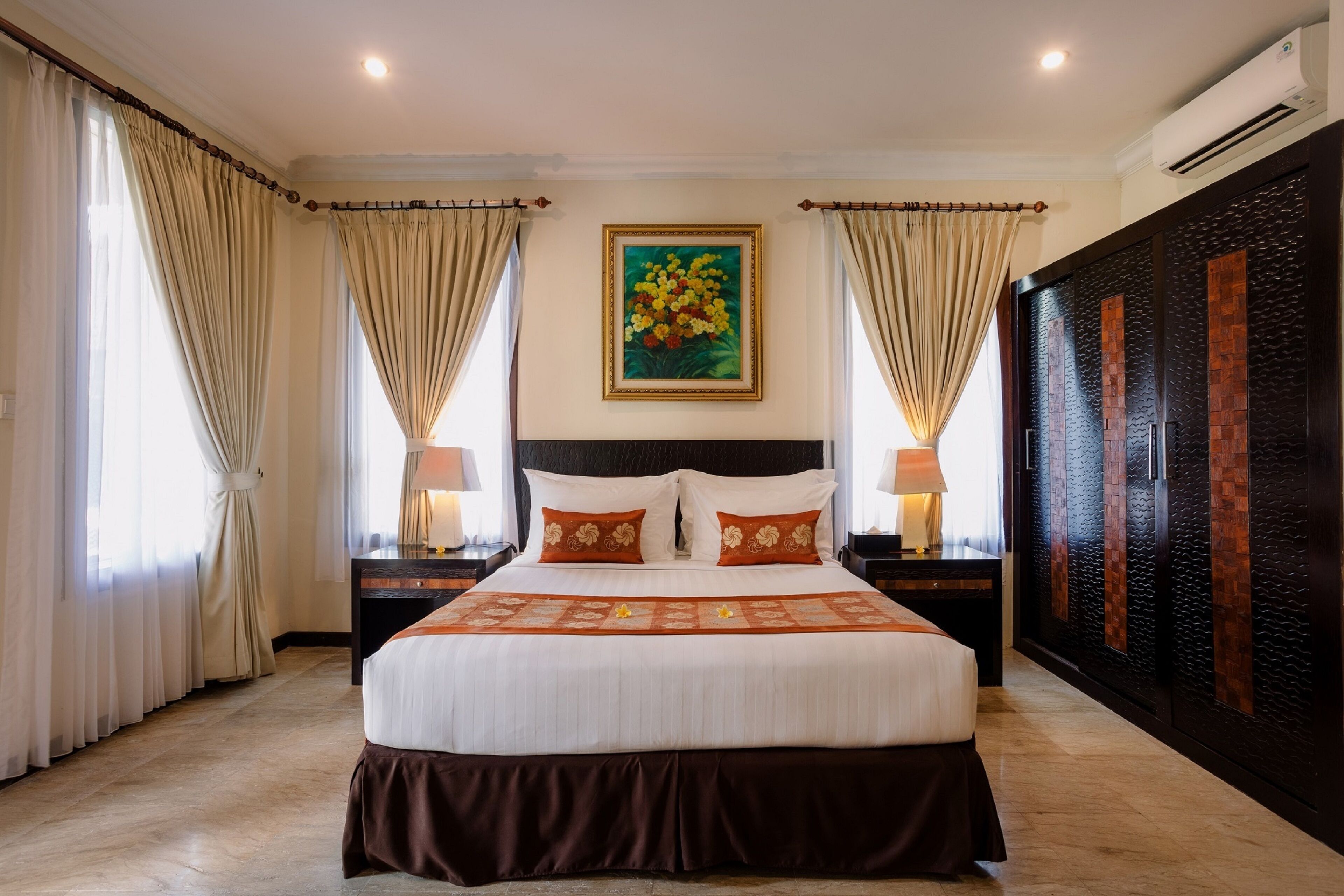 A spacious hotel room with a large bed, beige curtains, a painting above the bed, and a dark wooden wardrobe.