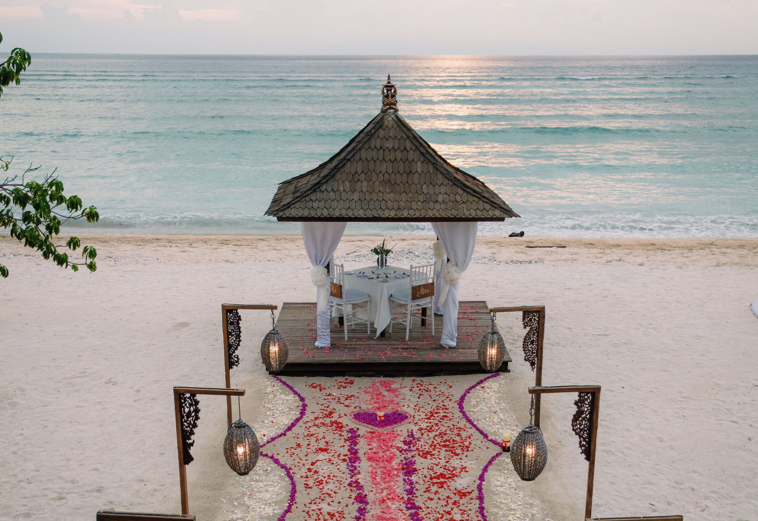 Une cérémonie de mariage organisée sur la plage, avec un gazebo, des chaises blanches et une table.