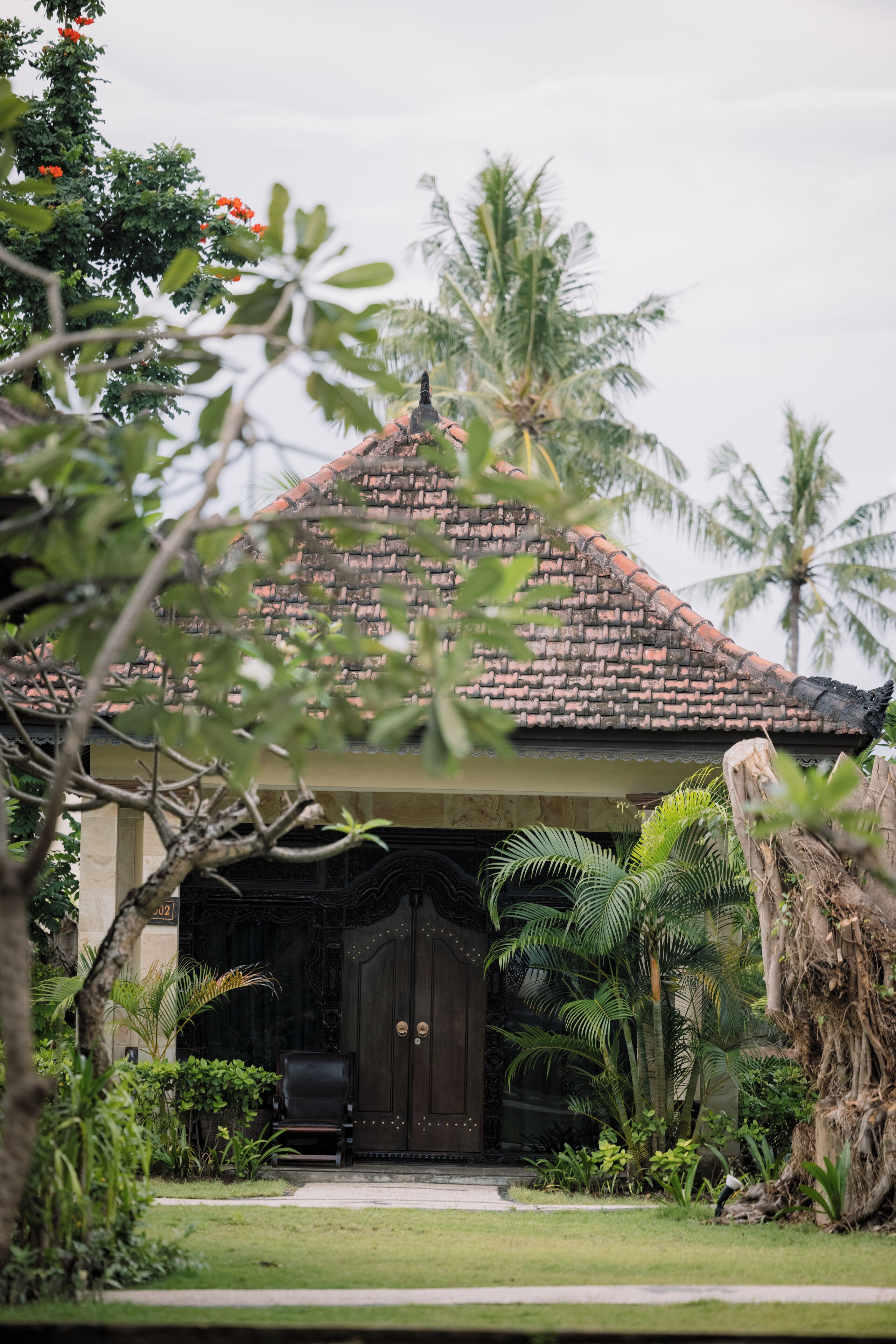 A traditional house with a tiled roof, surrounded by lush greenery and palm trees.