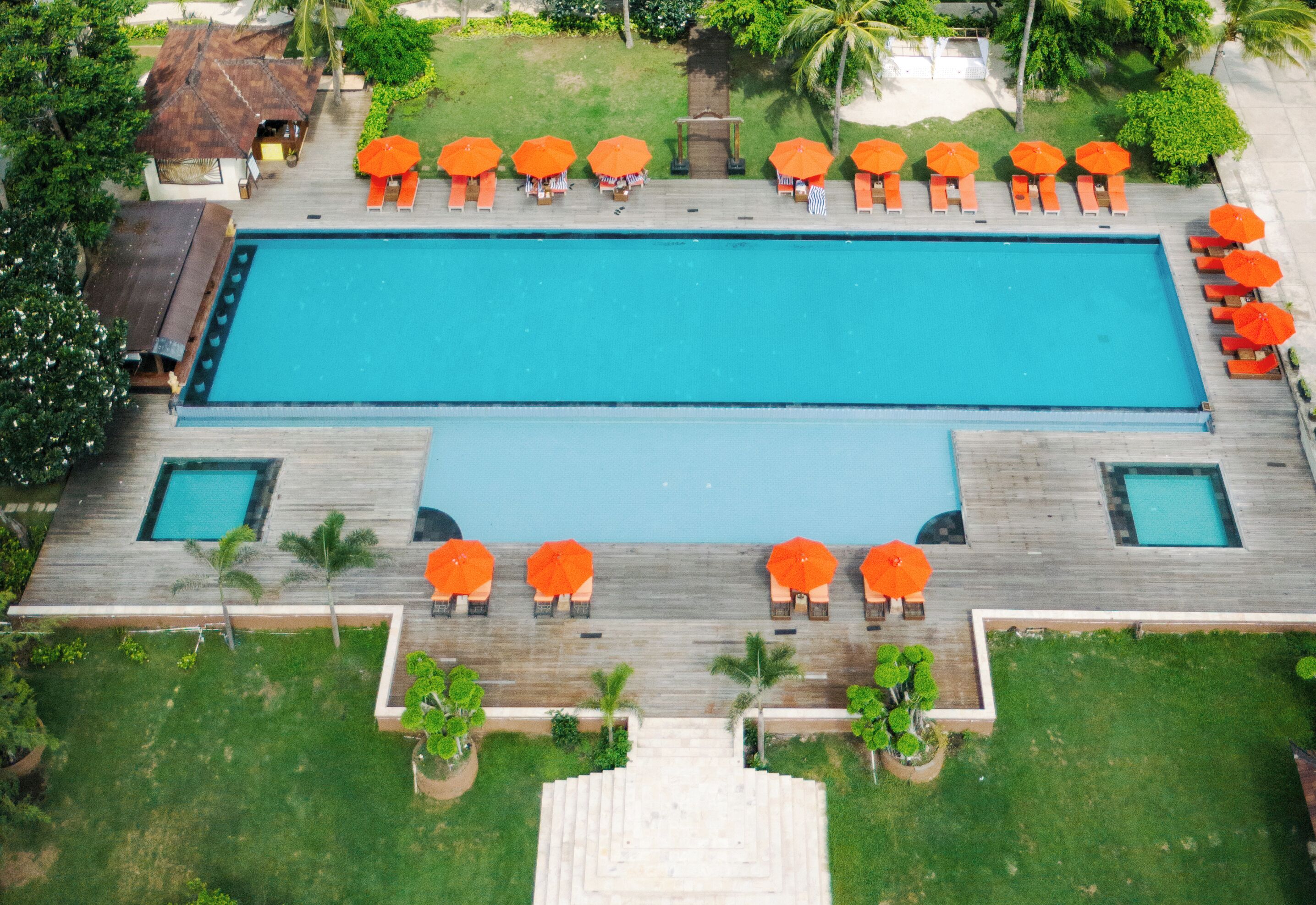 A rectangular swimming pool with a wooden deck, surrounded by lounge chairs and orange umbrellas.