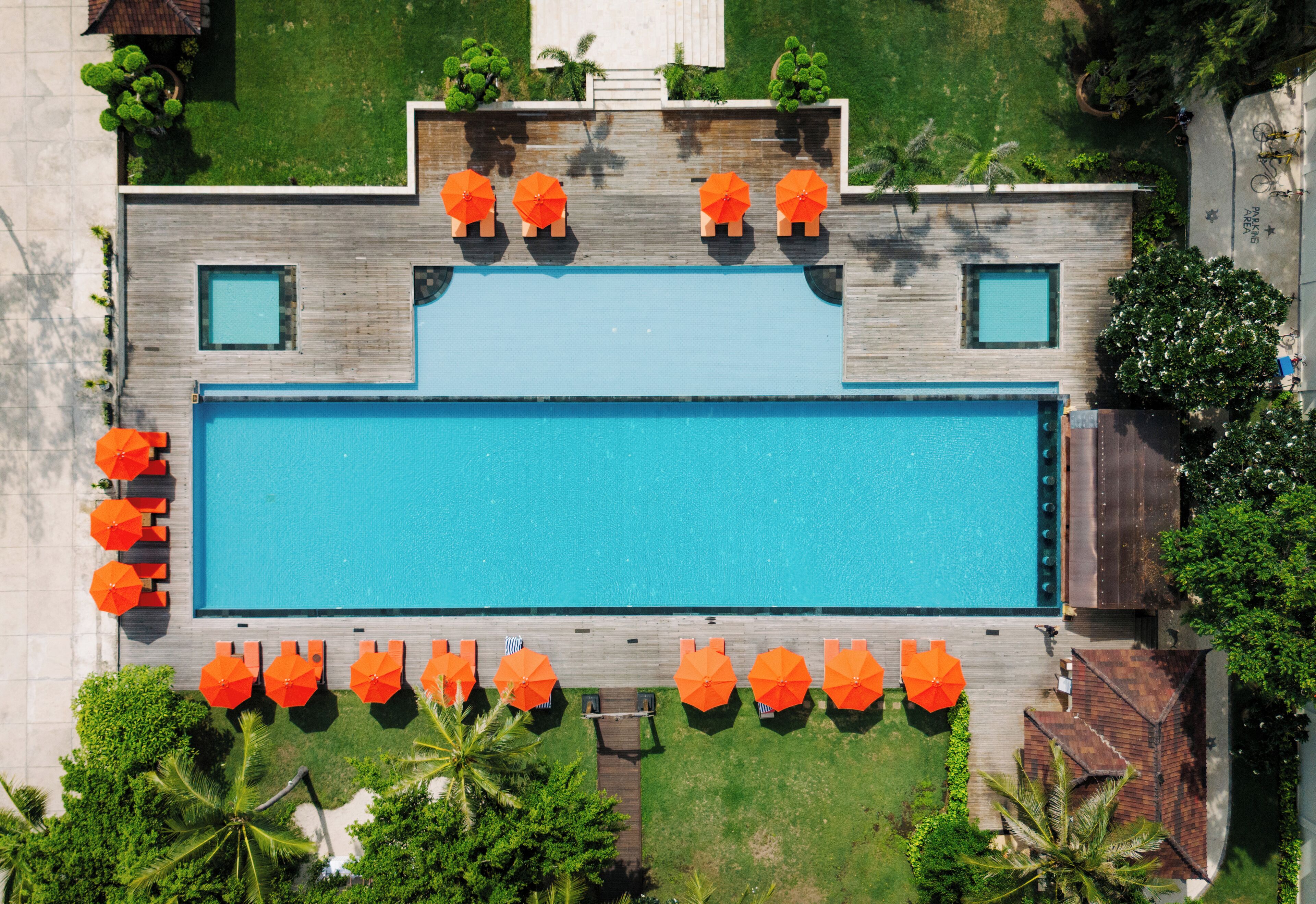 Vista aérea de una piscina rectangular con un deck de madera que la rodea, equipada con múltiples sombrillas naranjas para dar sombra.