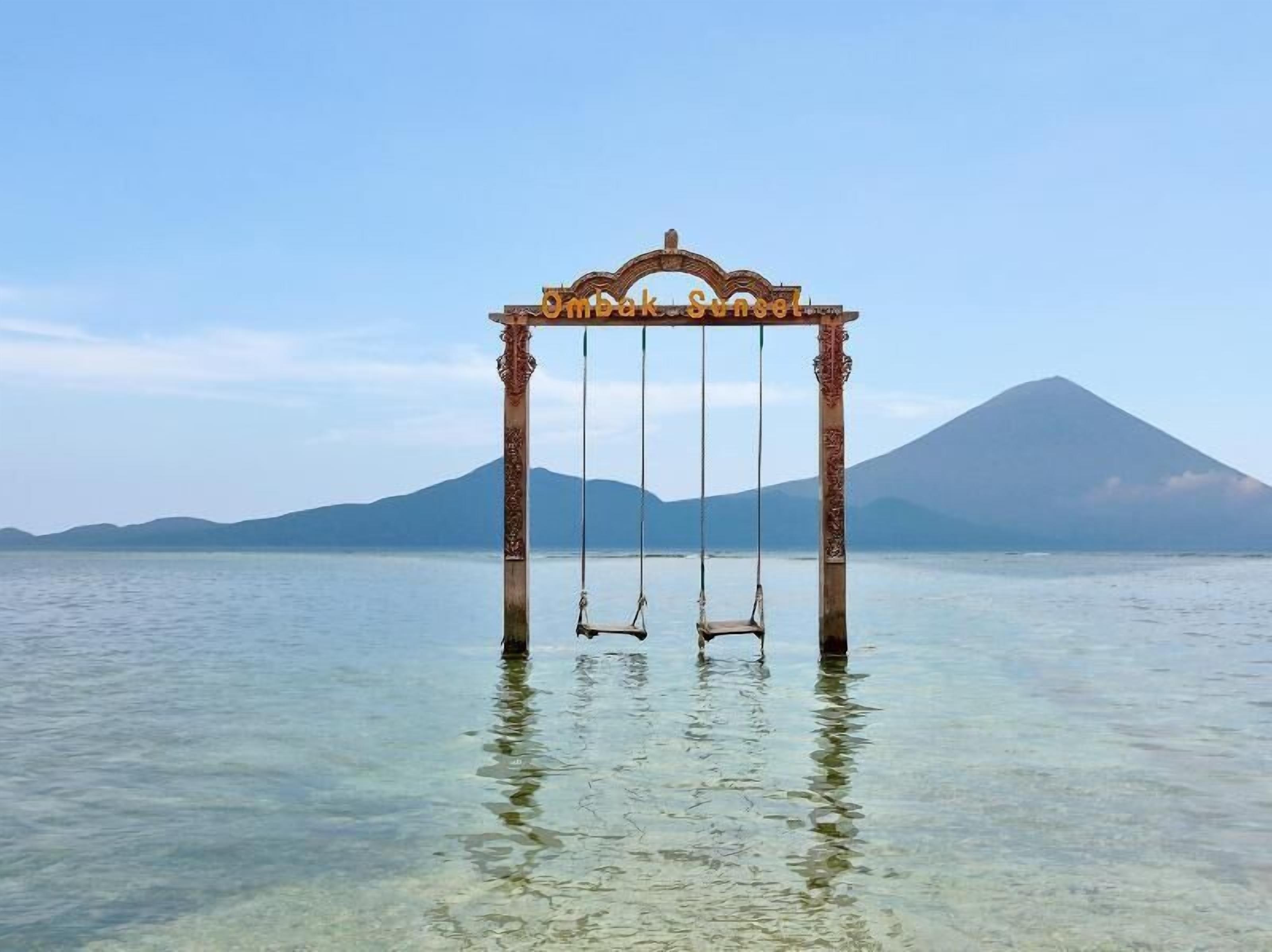 A swing set over water with a mountain in the background.