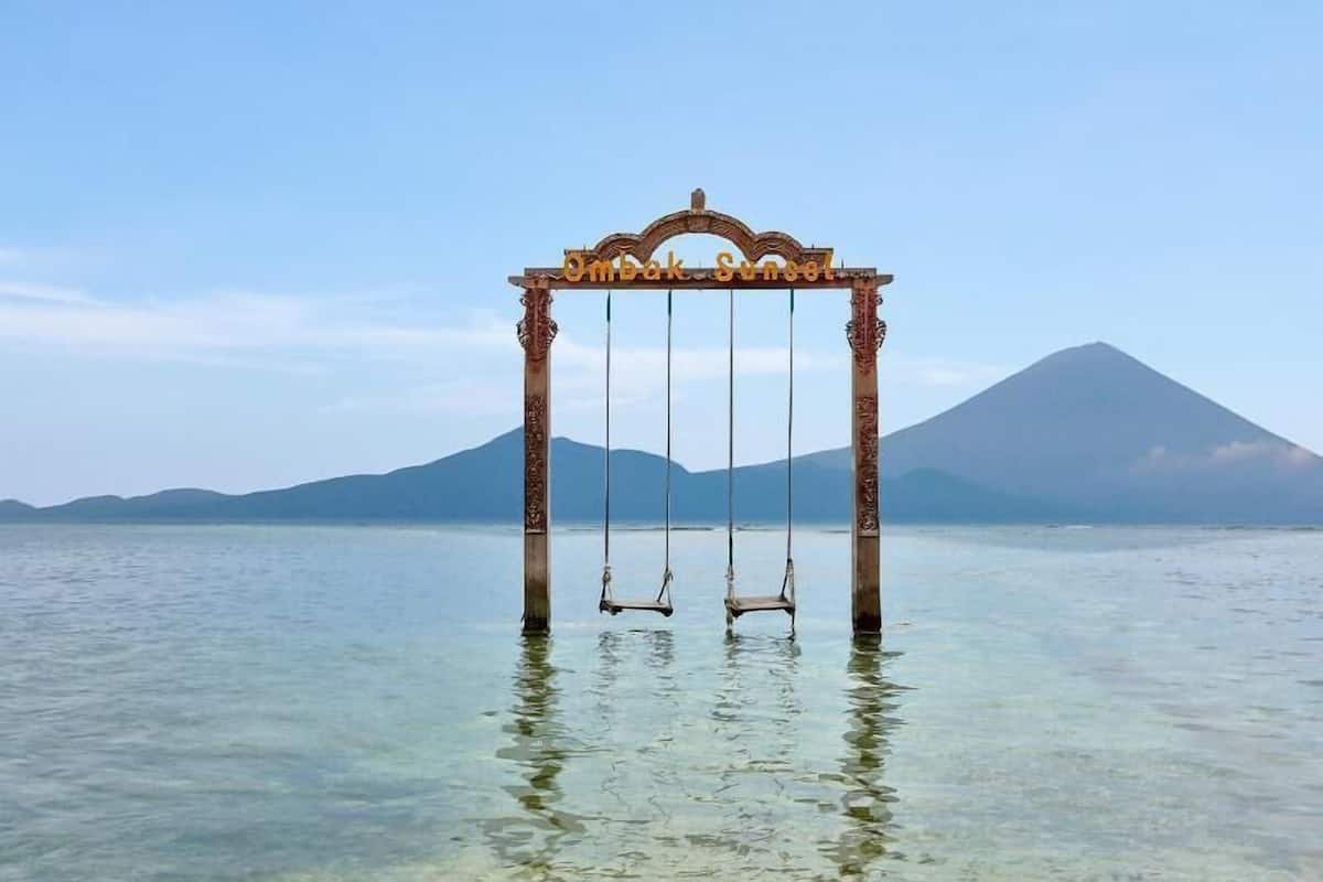 A swing set over water with a mountain in the background.