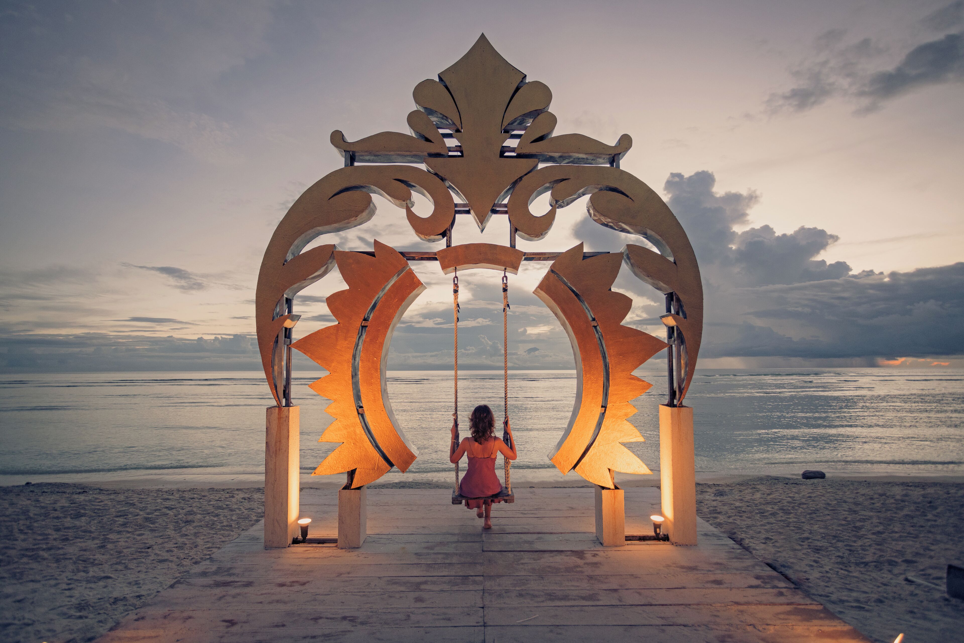 A woman on a swing with a decorative archway and a beach view in the background.