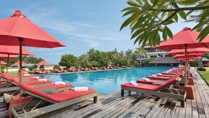 Ein Poolbereich mit Liegestühlen und roten Sonnenschirmen, einem Holzdeck und einem klaren blauen Pool.
