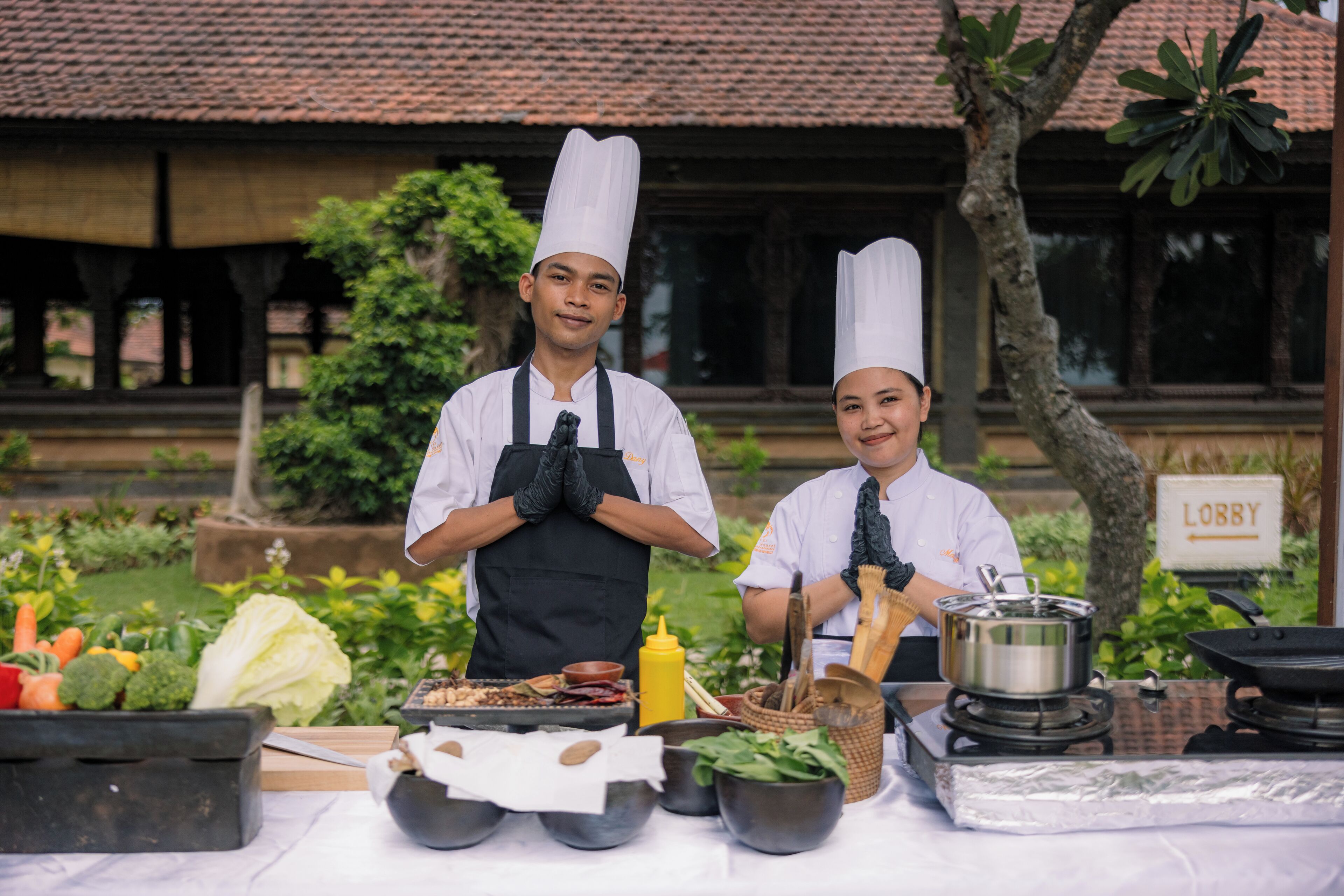 Two chefs standing in front of a table with cooking ingredients and utensils.
