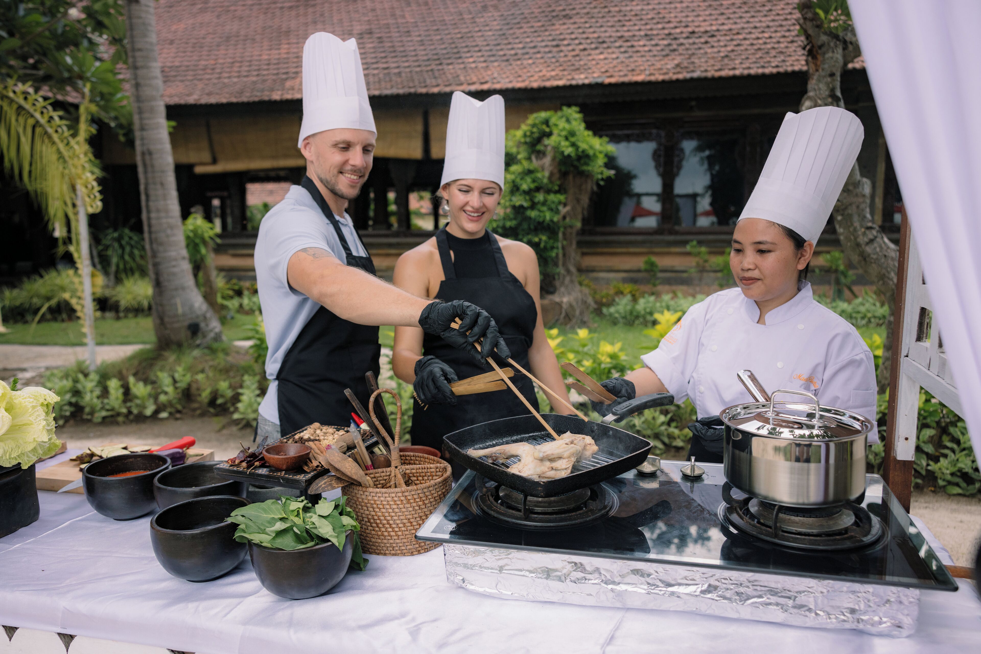 Un chef préparant des aliments à l’extérieur, à l’aide d’un gril, d’ustensiles de cuisine et de différents bols.